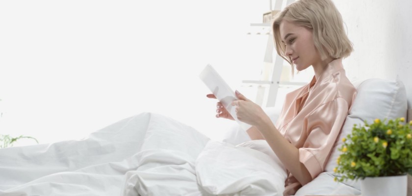 Donna bionda a letto che sta leggendo un articolo sul suo tablet