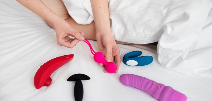 Vista ritagliata di una donna a letto e diversi giocattoli sessuali sopra le lenzuola